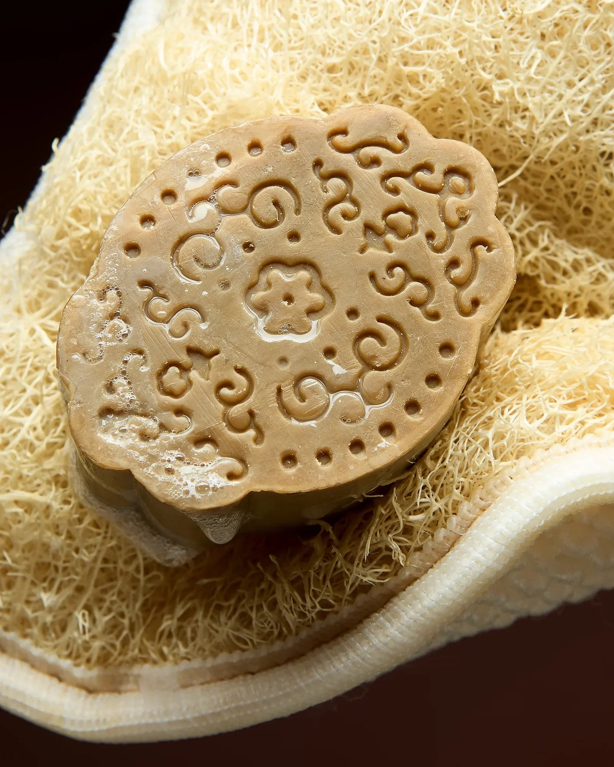 Savon d'Alep véritable estampillé du sceau du maître savonnier, posé sur un gant de loofah